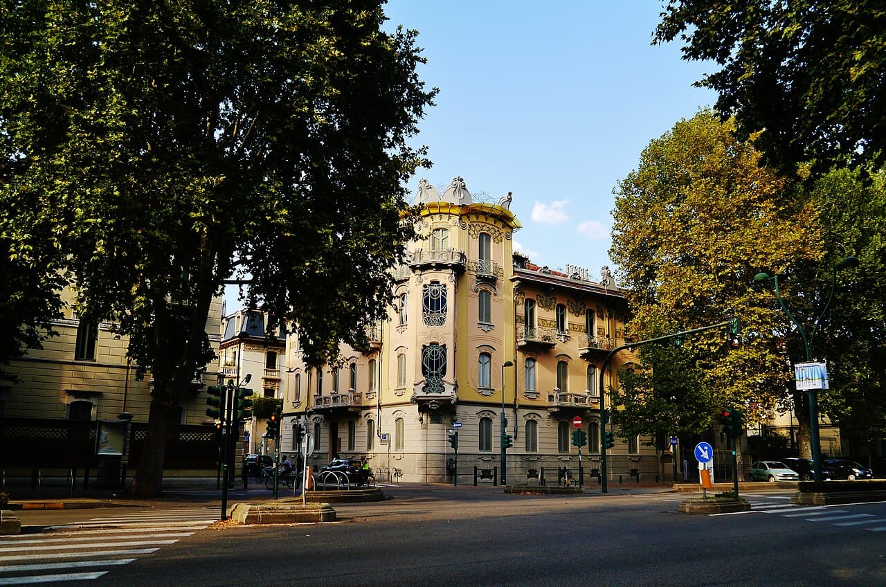Casa Fenoglio-Lafleur, an Art Nouveau corner building with a curved glazed bay and wrought-iron balconies, framed by plane trees